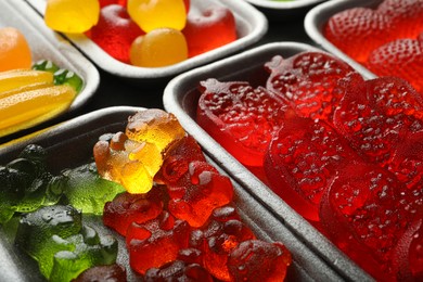 Photo of Different delicious gummy candies in containers, closeup