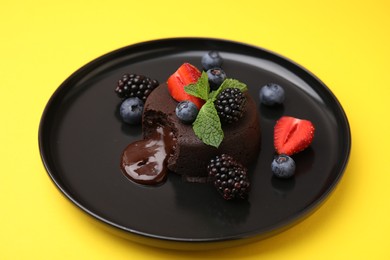 Plate with delicious chocolate fondant, berries and mint on yellow table