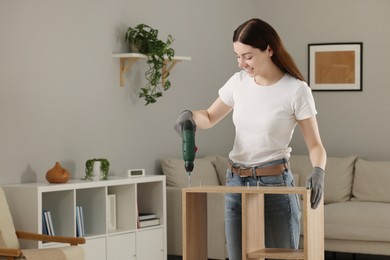 Young woman with electric screwdriver assembling furniture at home. Space for text