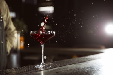 Photo of Glass of splashing cosmopolitan martini cocktail on bar counter. Space for text