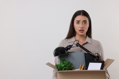 Photo of Unemployment problem. Confused woman with box of personal office belongings on white background, space for text