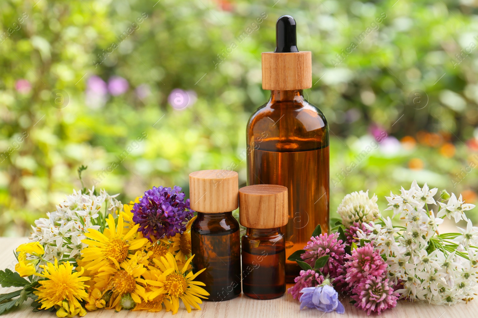 Photo of Bottles of essential oil and different flowers on white wooden table outdoors, closeup