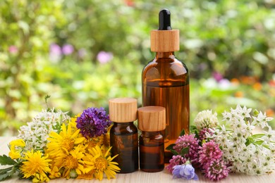 Bottles of essential oil and different flowers on white wooden table outdoors, closeup