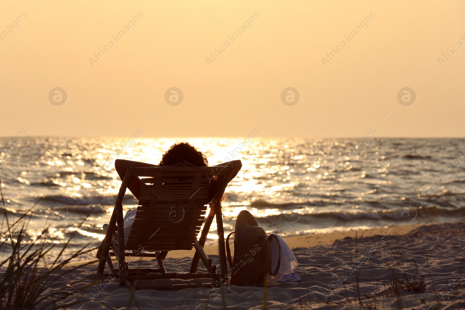 Photo of Woman resting in wooden sunbed on tropical beach at sunset