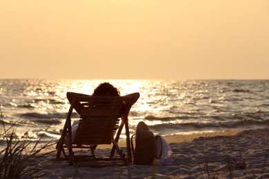 Woman resting in wooden sunbed on tropical beach at sunset