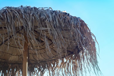 Photo of Beautiful straw beach umbrella against blue sky, closeup