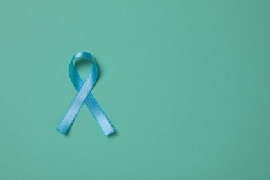 Light blue awareness ribbon on turquoise background, top view. Space for text