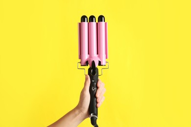Photo of Woman holding triple curling hair iron on yellow background, closeup