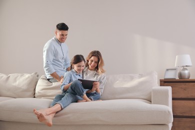 Photo of Family with little daughter using tablet on sofa in living room