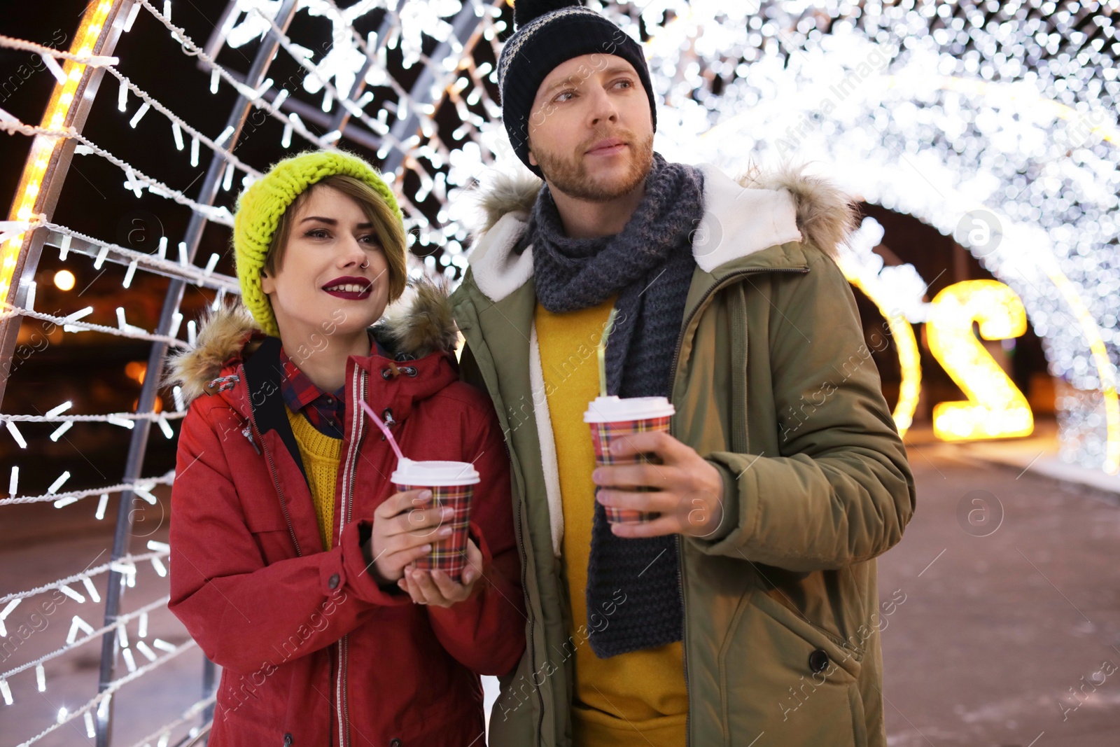 Photo of Young couple with cups of mulled wine at winter fair