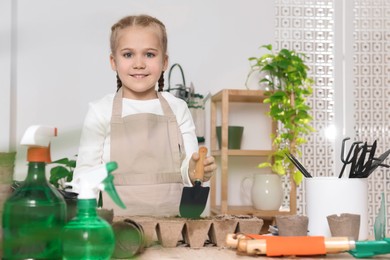 Photo of Little girl adding soil into peat pots at wooden table indoors. Growing vegetable seeds