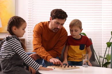 Father teaching his children how to play checkers at home