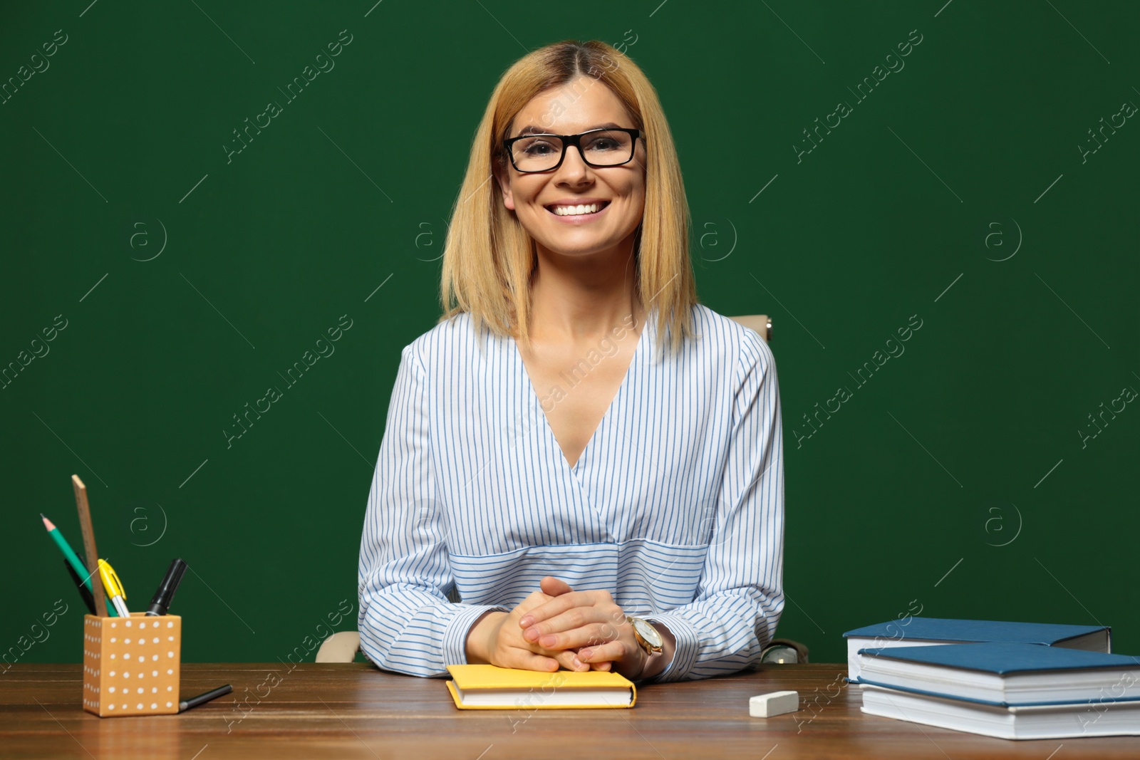 Photo of Portrait of beautiful teacher sitting at table near chalkboard