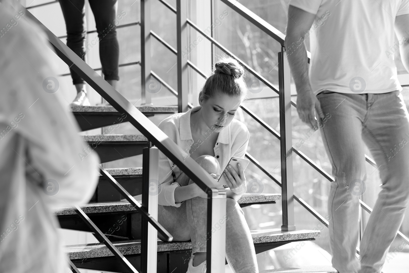 Photo of Young woman with smartphone sitting on stairs, toned in black and white. Alone among people