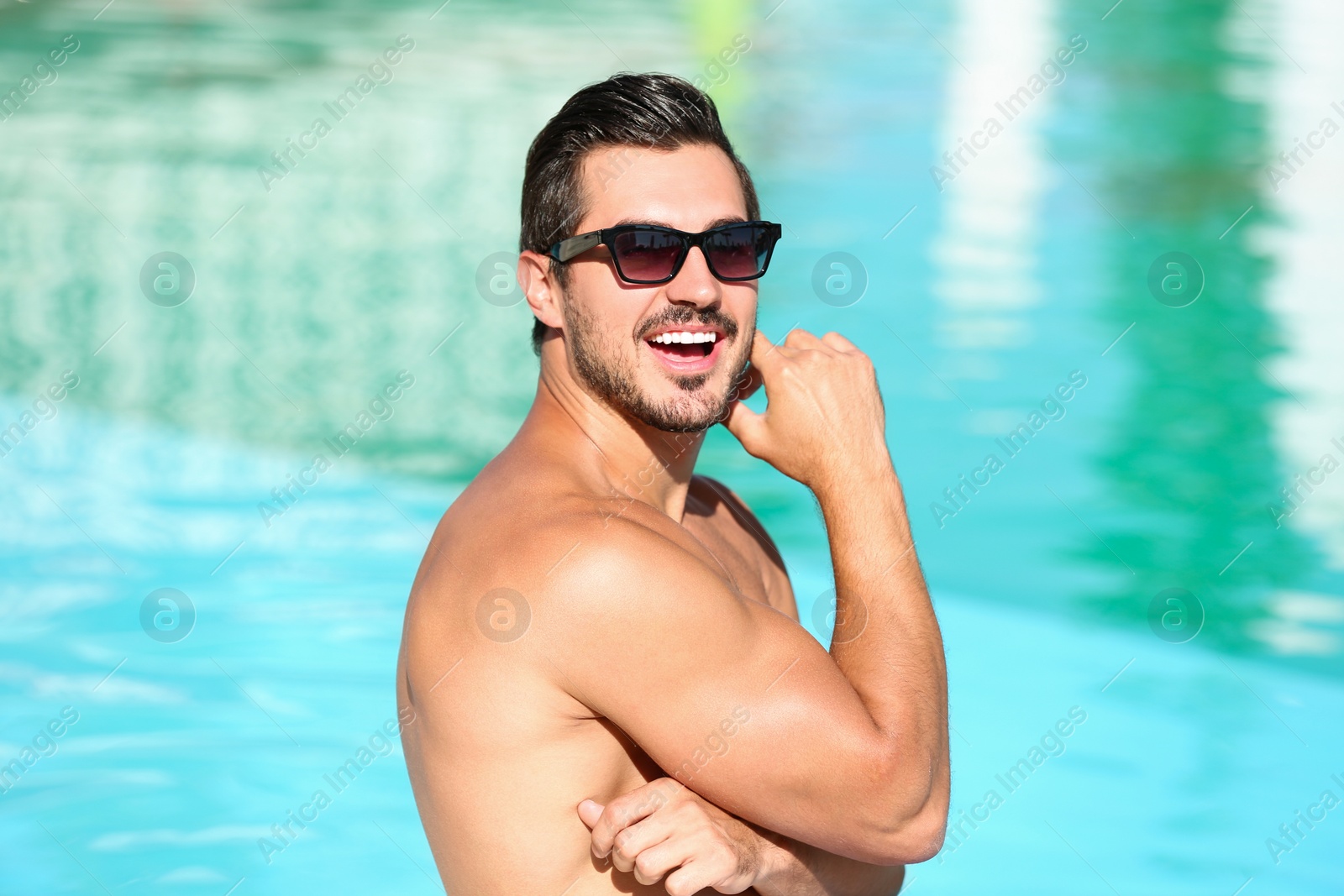 Photo of Handsome young man with sunglasses near swimming pool on sunny day