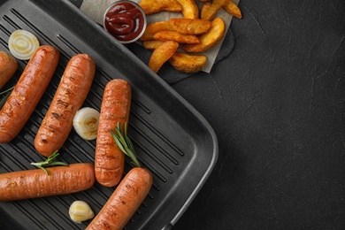 Photo of Flat lay composition with delicious sausages in grill pan on black table. Barbecue food