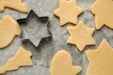 Photo of Raw Christmas cookies and cutter on baking parchment, top view
