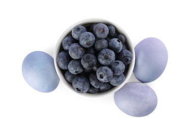 Photo of Colorful Easter eggs painted with natural dye and fresh blueberries on white background, top view