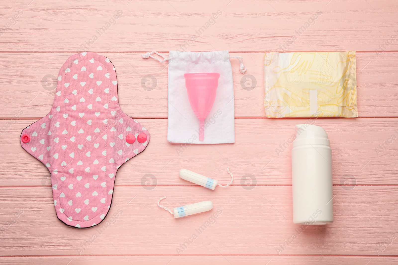 Photo of Cloth menstrual pad and other female hygiene products on pink wooden table, flat lay