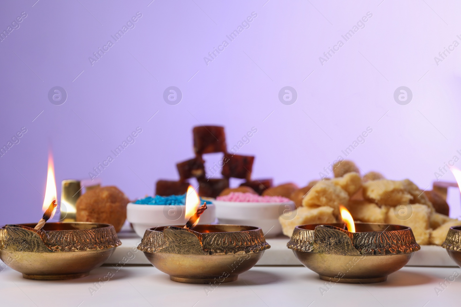 Photo of Happy Diwali. Diya lamps on white table against violet background, closeup