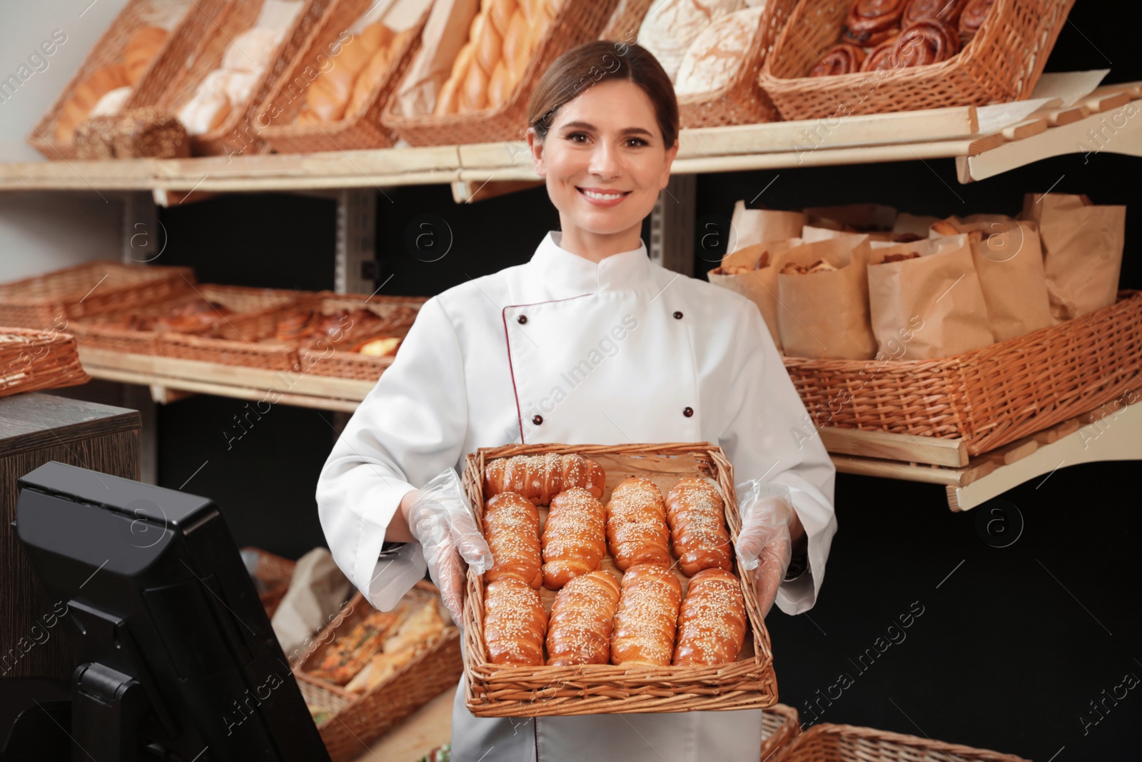 Photo of Professional baker holding tray with fresh buns in store