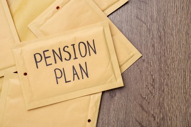 Photo of Envelope with words Pension Plan on wooden table, flat lay. Space for text