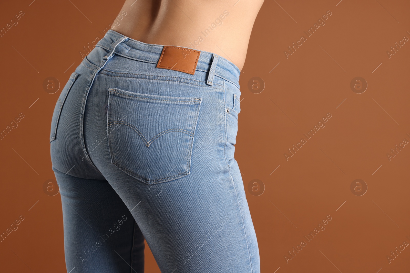 Photo of Woman wearing stylish light blue jeans on brown background, closeup. Space for text