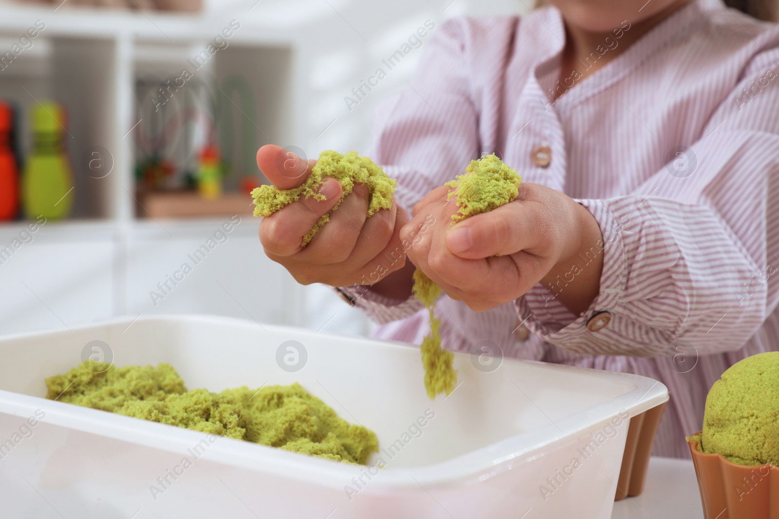 Photo of Little girl playing with bright kinetic sand at table indoors, closeup