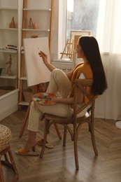 Photo of Beautiful young woman drawing on easel at home