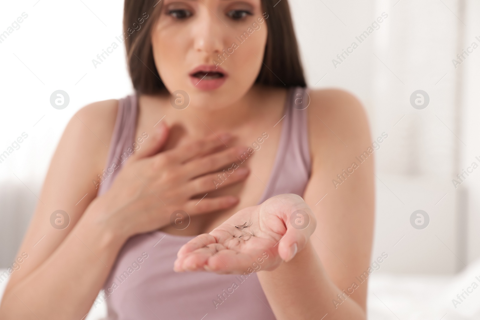 Photo of Beautiful woman holding fallen eyelashes in hand indoors, closeup
