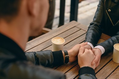 Photo of Lovely couple with coffee holding hands together at wooden table outdoors, closeup. Romantic date