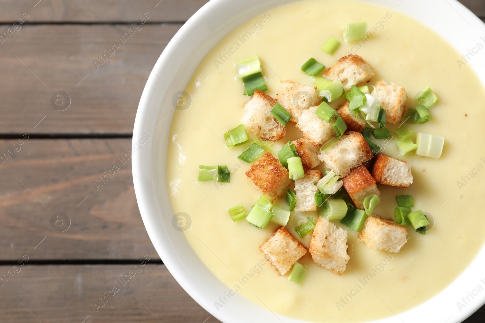 Photo of Tasty potato soup with croutons and green onion in bowl on wooden table, top view