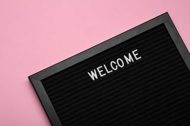 Photo of Black letter board with word Welcome on pink background, top view
