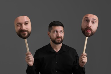 Man holding masks with his face showing different emotions on grey background. Balanced personality