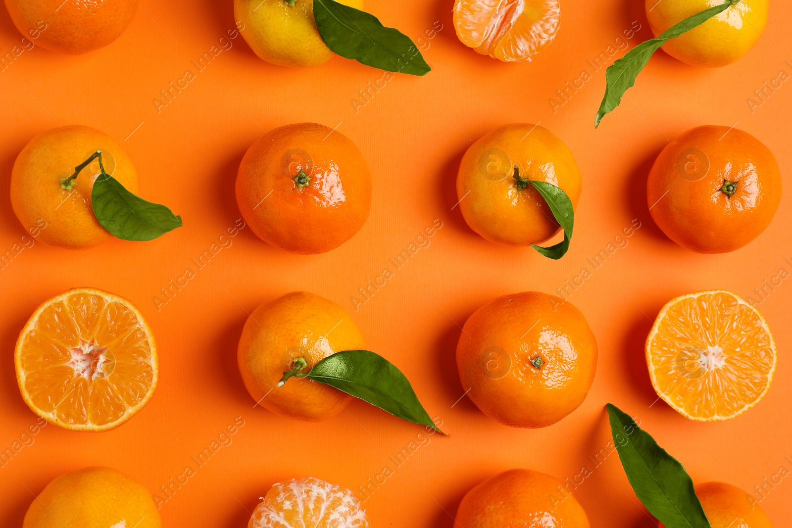 Photo of Delicious tangerines and green leaves on orange background, flat lay