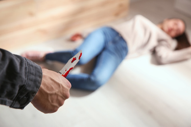 Photo of Man with bloody knife and his victim on floor indoors, closeup. Dangerous criminal