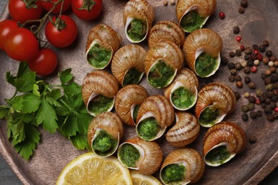 Photo of Delicious cooked snails with lemon, tomatoes and parsley on wooden board, top view