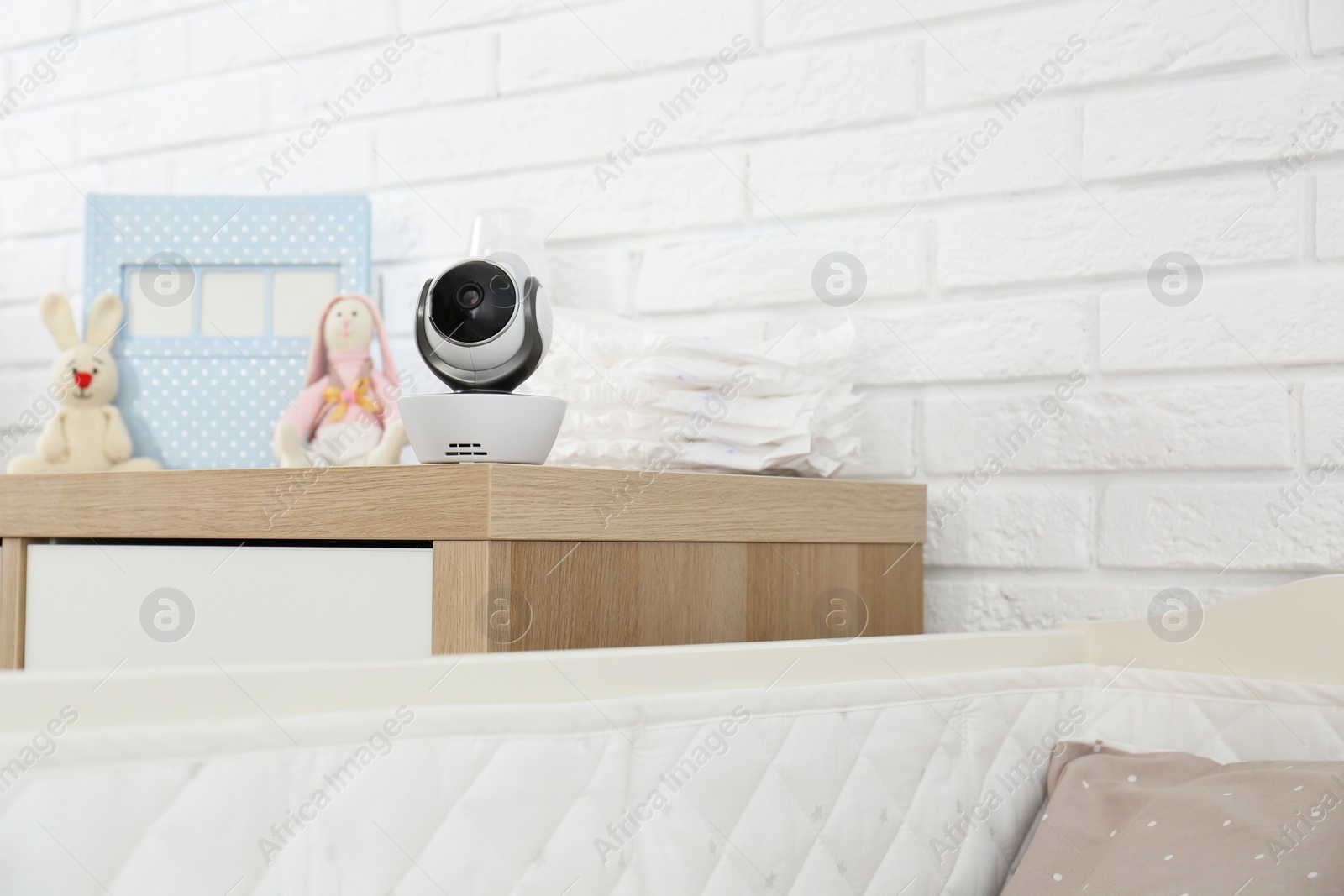 Photo of Baby camera and accessories on chest of drawers near crib in room, space for text. Video nanny