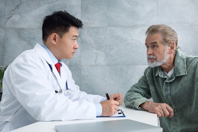 Doctor consulting senior patient at white table in clinic