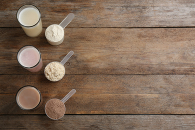 Protein shakes and powder on wooden table, flat lay. Space for text