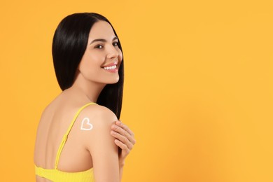 Photo of Young woman with heart drawn with sunscreen against orange background. Space for text
