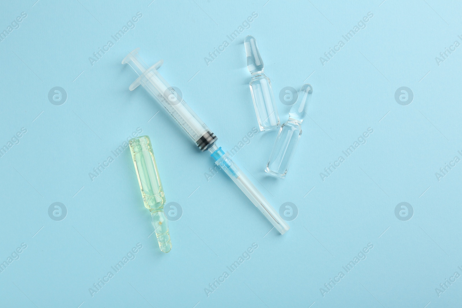 Photo of Glass ampoules with liquid and syringe on light blue background, flat lay