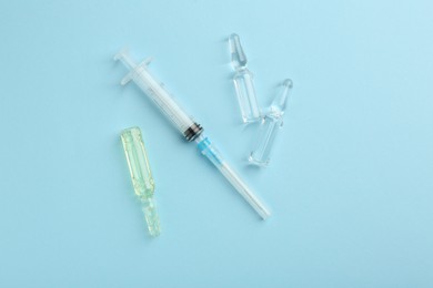 Photo of Glass ampoules with liquid and syringe on light blue background, flat lay