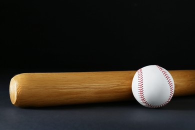 Photo of Wooden baseball bat and ball on black background, space for text. Sports equipment