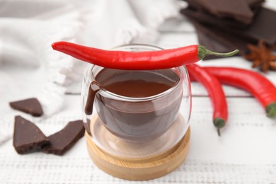 Glass of hot chocolate with chili pepper on white wooden table, closeup
