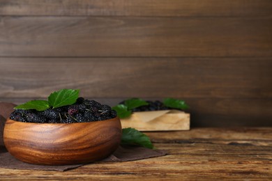 Photo of Fresh ripe black mulberries in bowl on wooden table. Space for text