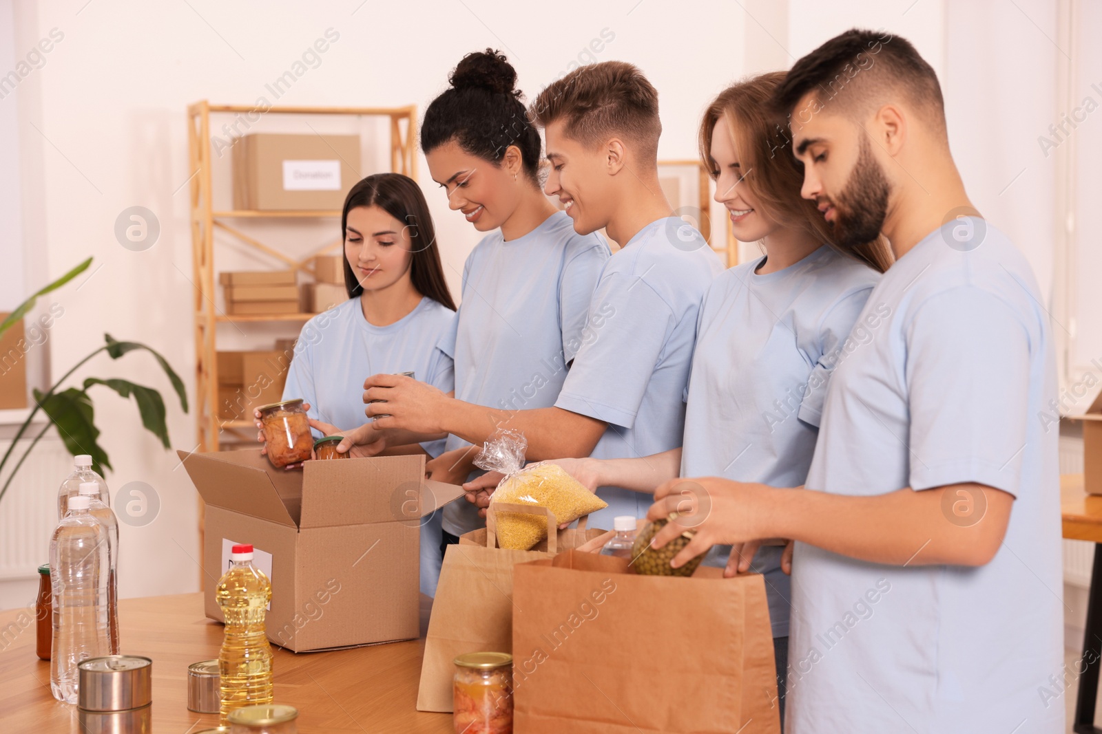 Photo of Group of volunteers packing food products at table in warehouse