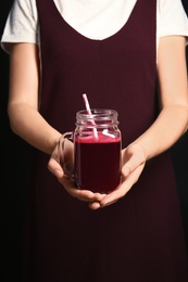 Photo of Woman with mason jar of beet smoothie on black background, closeup