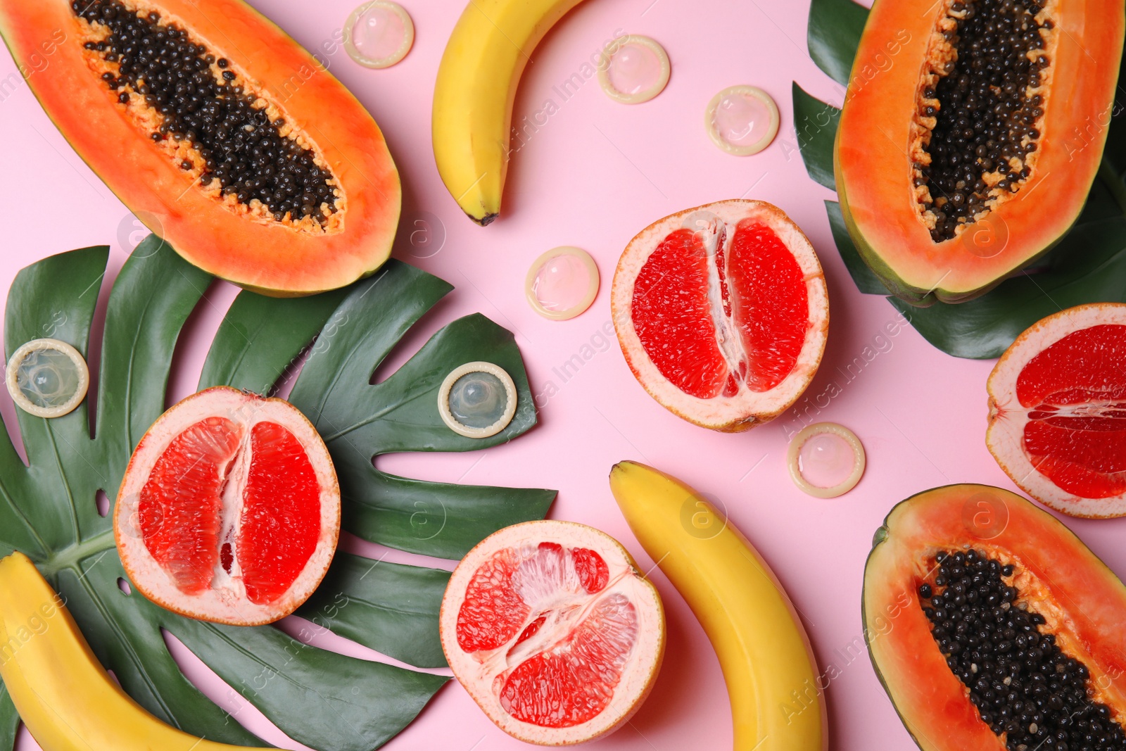 Photo of Flat lay composition with condoms and exotic fruits on pink background. Erotic concept