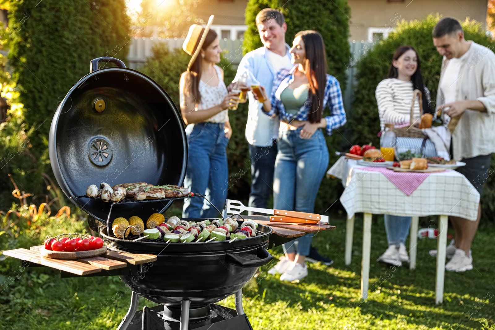 Photo of Group of friends having party outdoors. Focus on barbecue grill with food
